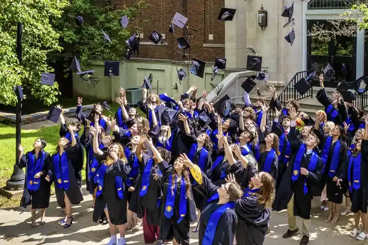 Craft Academy students in graduation regalia tossing their mortarboard hats