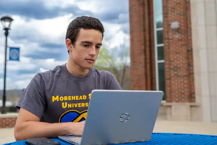 male student working on a laptop outside the Adron Doran University Center