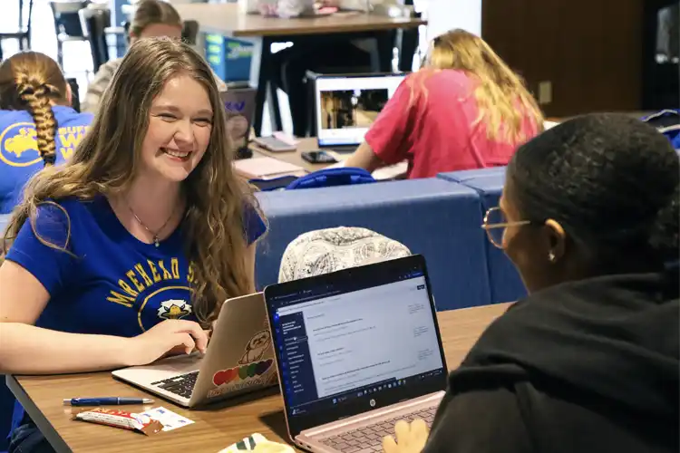 two students at a table talking with a laptop