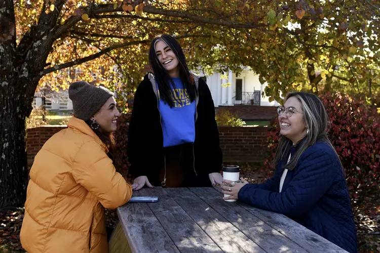 3 students sit outside on MSU campus with textbook.
