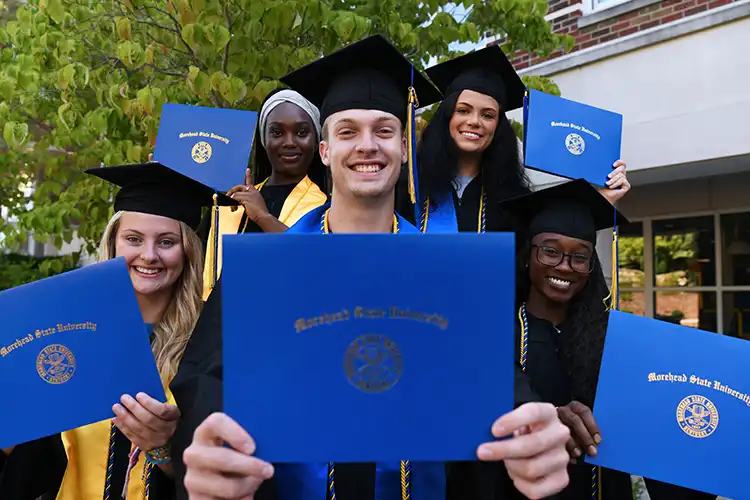5 students in cap and gowns hold MSU diplomas