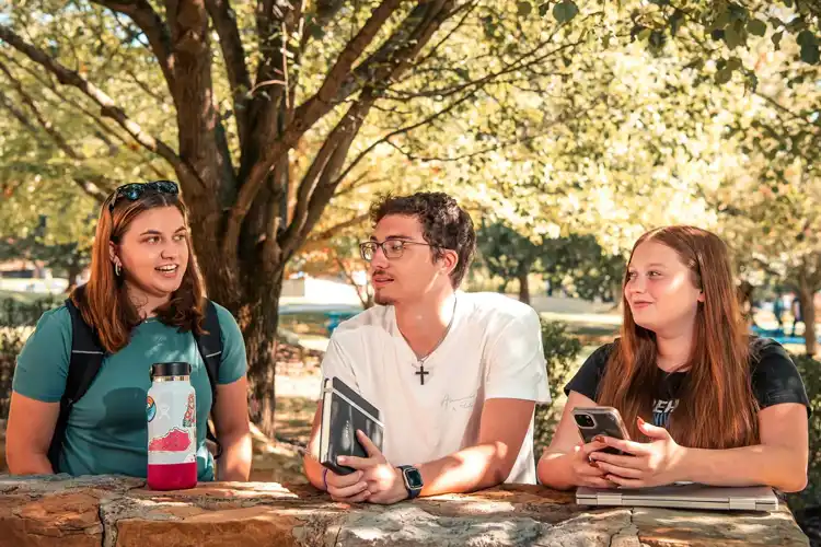 3 Students talking near a rock wall on campus